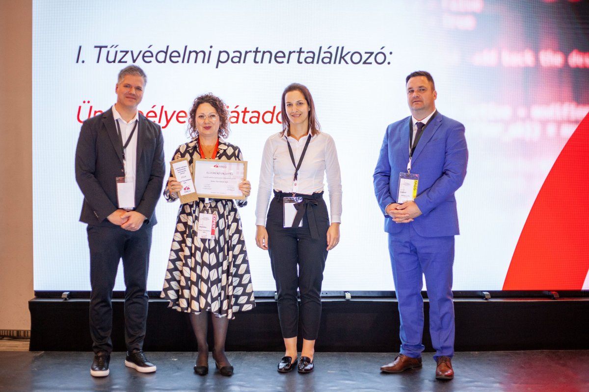 Négy fő a színpadon az I. Tűzvédelmi partnertalálkozó felirat előtt, középen egy hölgy elismerő oklevelet tart