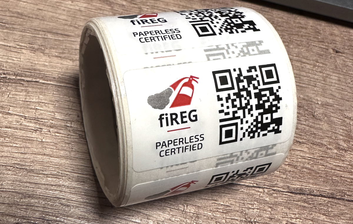 fiREG Paperless Certified feliratú, QR-kódos matricatekercs egy fa asztalon