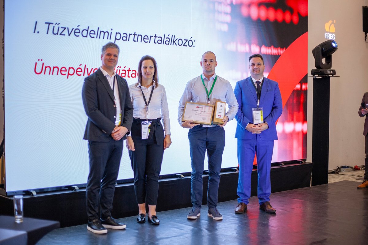 Négyen állnak a színpadon az I. Tűzvédelmi partnertalálkozó ünnepélyes díjátadóján, egyikük oklevelet tart